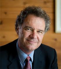 smiling man in a black suit in front of a wooden wall
