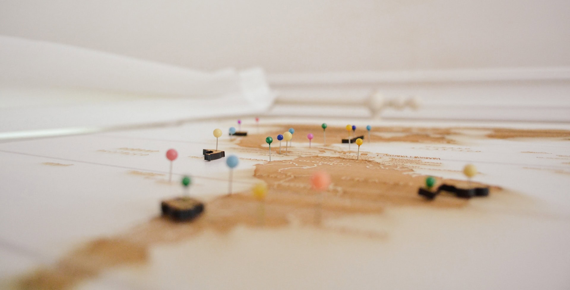 Map of the Americas with colorful pins in different locations from an extreme oblique angle on a white background.
