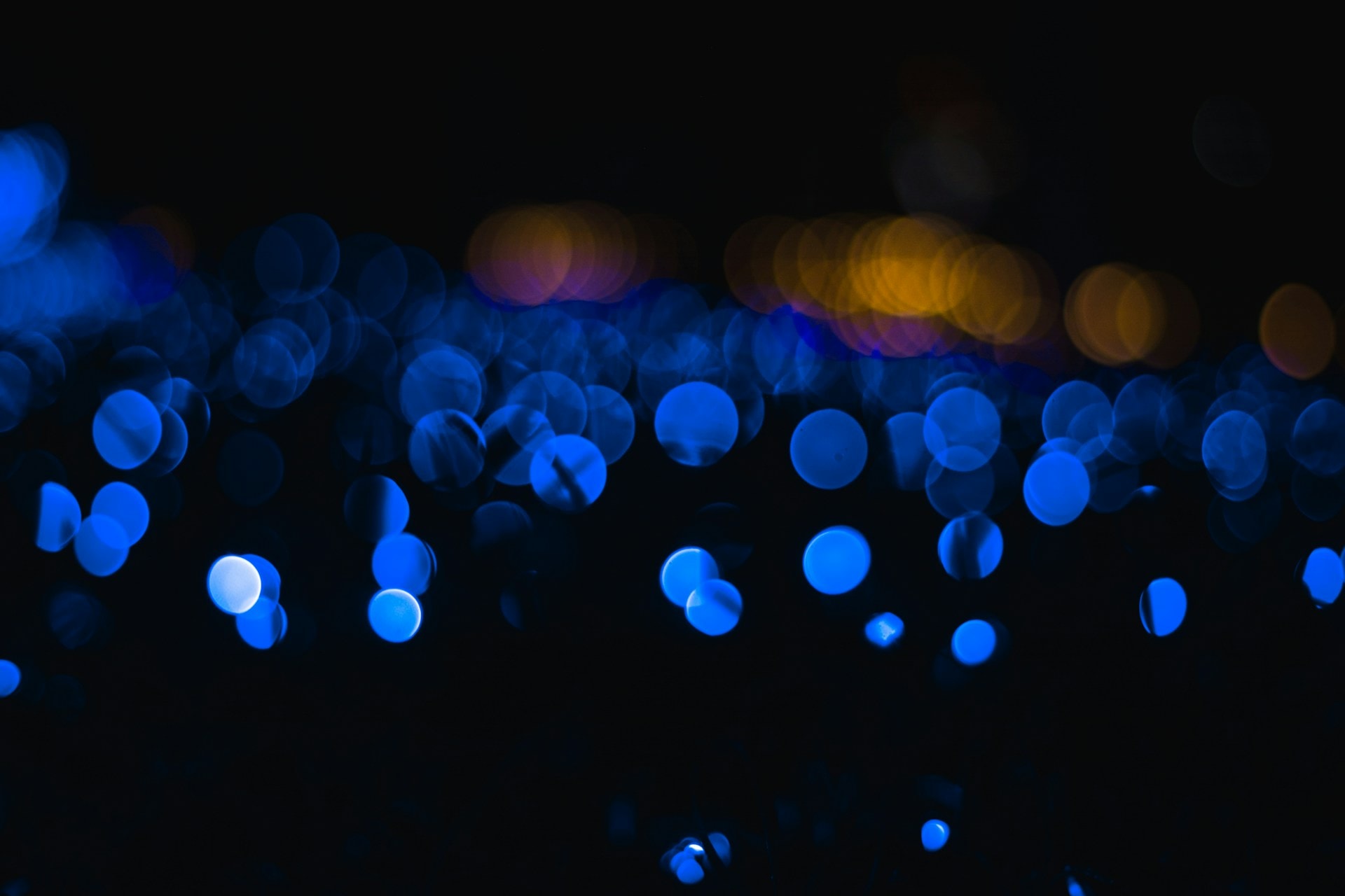 Black background with clusters of translucent and overlapping dark blue, pink, and orange dots of varying sizes, some of which have blurred edges.