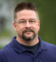 man with a goatee staring into camera in dark blue polo