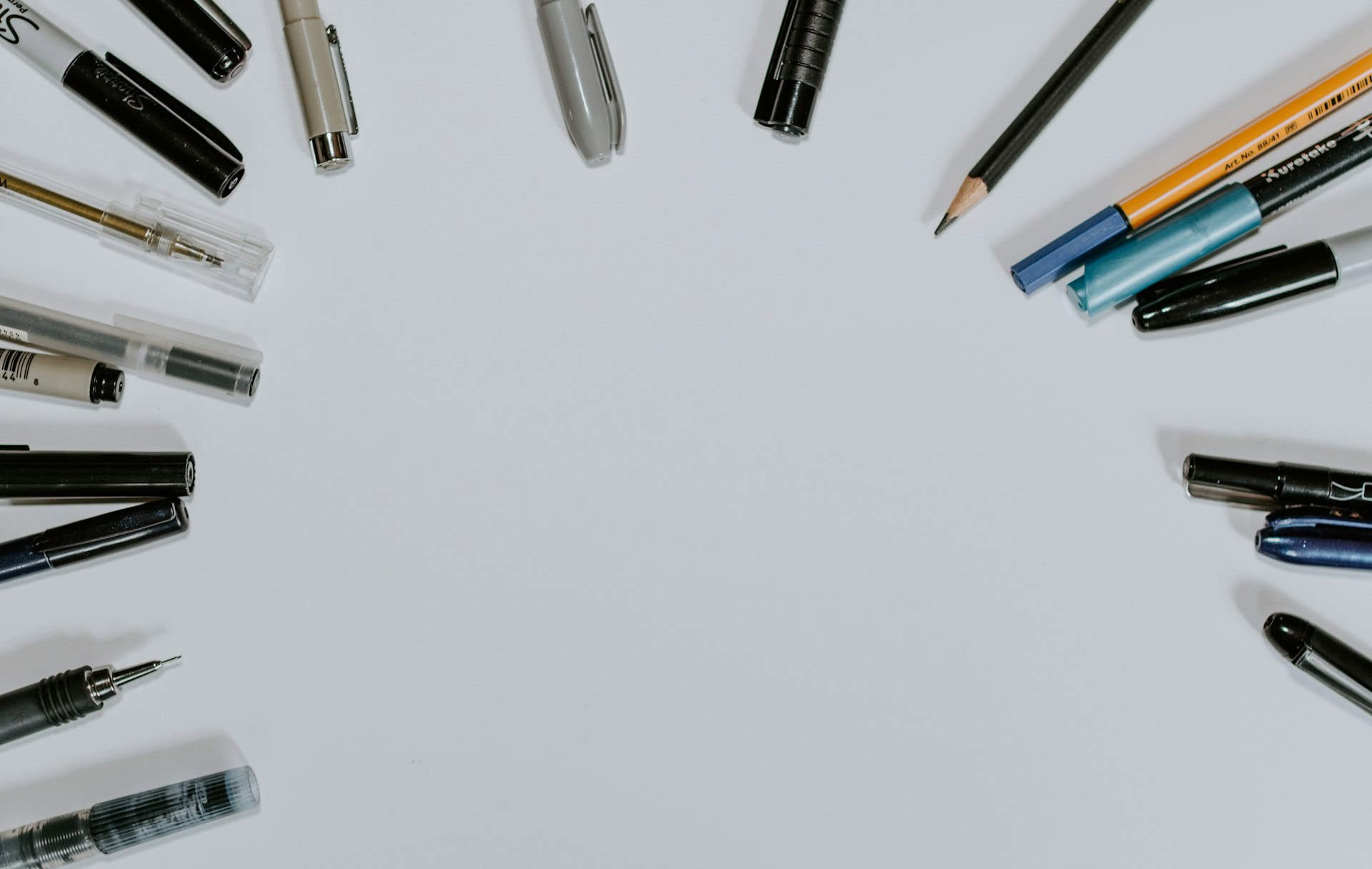 Pens of various neutral colors arranged in a partial circle, pointing towards the center of the circle.